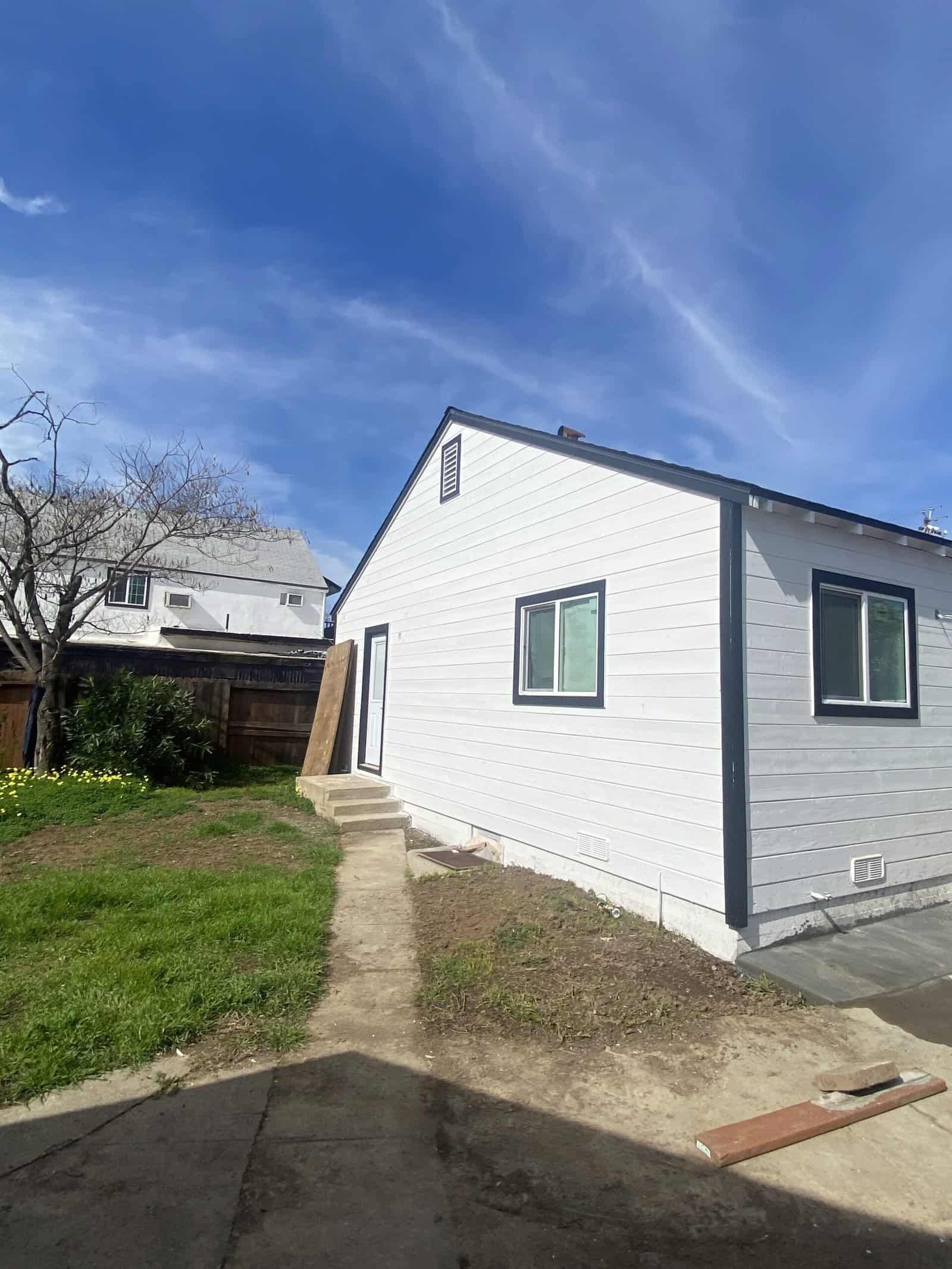 White house with black trim and a small front yard under a bright blue sky.